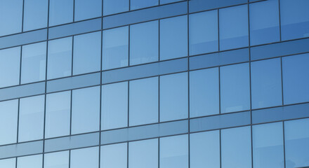 Modern glass building facade reflecting clear blue sky with geometric window patterns and minimalist urban architecture design