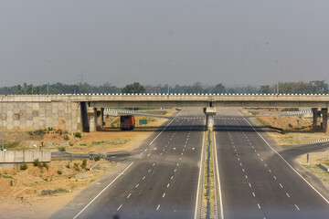 Empty multi-lane highway passing under a concrete overbridge, modern road infrastructure, transportation concept, clear sky, travel route, urban development, and minimal traffic scene in Assam.