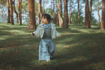 Adorable little Asian girl in a fleece jacket exploring a scenic pine forest while holding a pine cone for outdoor adventure and childhood travel concept
