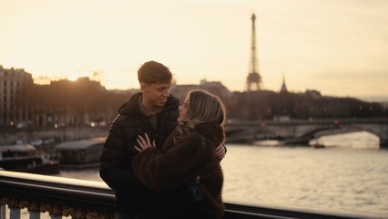 A romantic couple embraces in Paris France with the Eiffel Tower visible in the background at sunset. This image conveys love affection and the allure of European travel and tourism.
