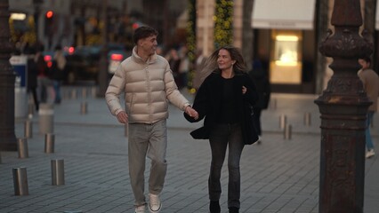 A young couple walks hand-in-hand down a cobblestone street in Paris France during the evening The...