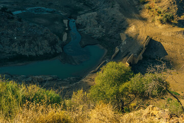 Valley with ancient stone bridge, river stream and green vegetation in sunlight. Seen from above. Almogia, Malaga, Andalusia, Spain.