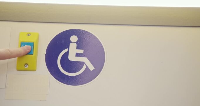 Close up of passenger on bus pressing disabled stop button. Passengers traveling by bus, bus driving, stopping. Concept of modern reality, everyday routine and urban atmosphere.