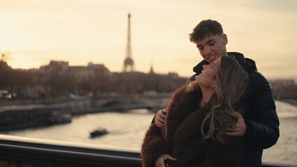 A romantic couple embraces with the Eiffel Tower in the background during sunset in Paris France. This image can be used for travel tourism and relationship themes. © 4kclips