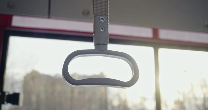 Front view of grey bus handle on empty bus. Bus topping with handle for holding, panorama os sunny evening city on background. Concept of public transport and urban settings,