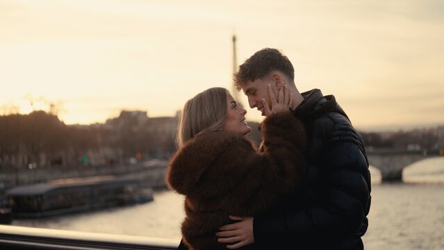 A romantic couple embraces with the Eiffel Tower in the background in Paris France at sunset. This image is suitable for travel and tourism concepts and Valentine's Day celebrations.