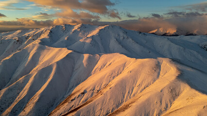 Snow covered mountain range bathed in golden sunlight during sunrise or sunset