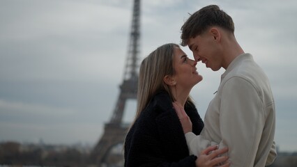 A young couple embraces romantically in Paris France with the Eiffel Tower in the background. This image is perfect for travel tourism and European vacation concepts.