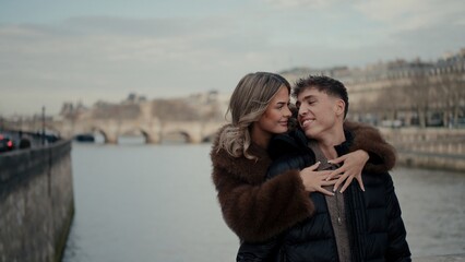 A romantic couple embraces on a bridge in Paris France with the Seine River and cityscape in the...