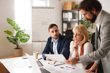 Business team meets in office to discuss project. Team members analyze charts and documents, share ideas, and plan future strategies for success.