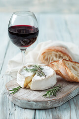 Soft cheese such as camembert or brie with rosemary, sliced baguette and a glass of red wine. Elegant appetizer and French cuisine concept.