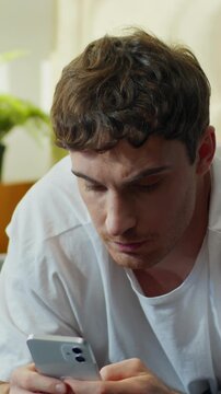 Unhappy Caucasian man lying in bed using smartphone at home worried confused male checking phone problem guy frowning mobile banking fraud spam crash app social media error lost connection breakdown