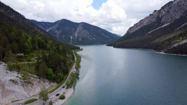 Aerial view of the majestic Plansee lake surrounded by steep mountains and a scenic road in Tyrol, Austria.