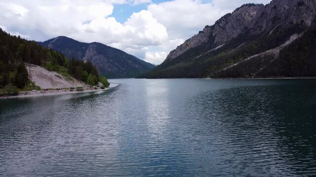 Aerial view of the majestic Plansee lake surrounded by steep mountains and a scenic road in Tyrol, Austria.