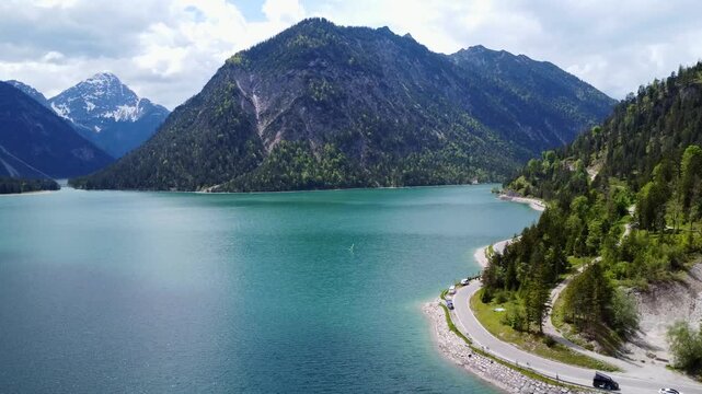 Aerial view of a winding road along the turquoise Lake Plansee in the Tyrolean Alps, Austria.