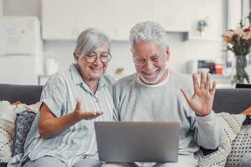 Fototapeta premium Cheerful mature married family couple talking on video call on laptop, watching funny movie with internet media TV service, enjoying leisure on couch with gadget, relaxing at home, laughing