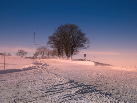 Asphalt road in dangerous winter conditions among snow covered scenic landscape, solitary tree