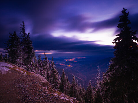 Harsh scenic landscape of Jeseniky mountains with spruce trees covered with rime,clouds and a view on the city in the evening