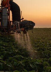 Tractor spraying crops in a lush green field at sunset.