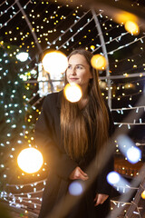 Happy young woman against the backdrop of festive Christmas lights