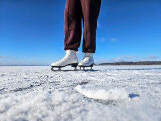 Female figure skater wearing white skates stands on smooth ice surface, showcasing balance and elegance in winter sports, with serene natural backdrop enhancing the scene