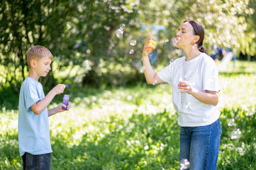 Mother and teen boy having fun blowing soap bubbles in summer park