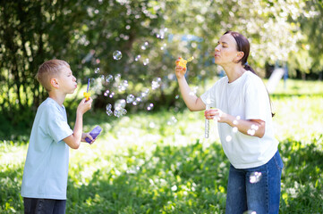 Mother and teenage son playing with soap bubbles in sunny park