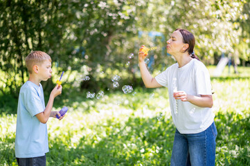 Mother and teen boy having fun blowing soap bubbles in summer park