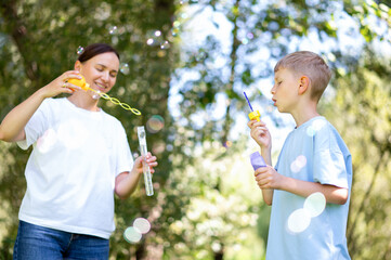 Blowing soap bubbles together: mother and teenage boy in park
