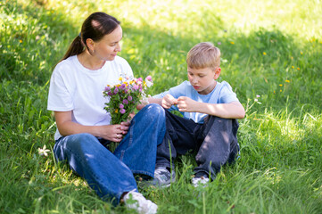 Teen boy giving mother bouquet of wildflowers on green lawn, family bonding outdoors