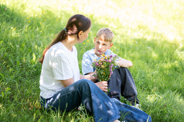 Mother holding bouquet of wildflowers on lawn with teen son in sunny summer day