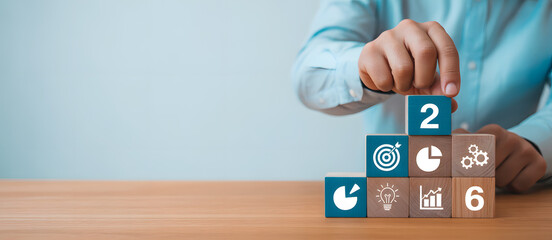 Close up of a person s hands stacking wooden blocks with business icons and numbers forming a pyramid shape on a wooden desk representing growth and strategy