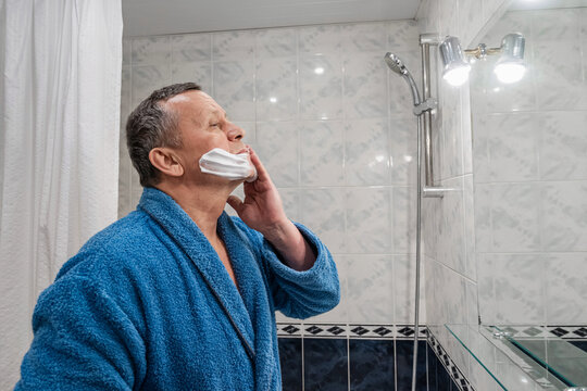 Adult man applying shaving foam on face while looking in mirror. Morning grooming routine and male skincare concept. Morning Shaving Routine - Powered by Adobe