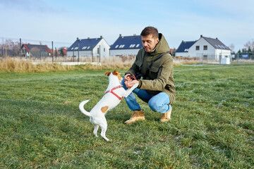 Man crouching and training small dog on green grass using hands in open field