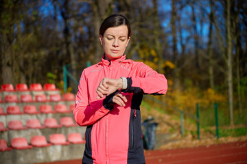 Woman wearing sports jacket checking smartwatch while standing on running track