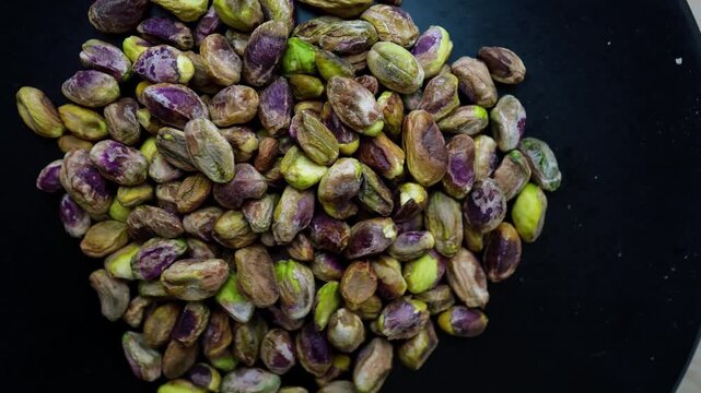 Close-up of unshelled pistachios on a dark surface