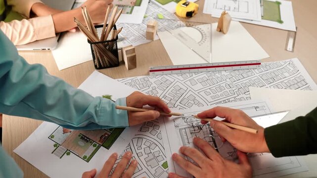 Smart architect and safety engineer discussion about building blueprint on table with architectural document, measurement tools and wooden block scatter around at modern office. Closeup. Delineation.