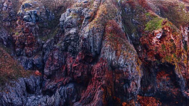 Cliffs rise above the sea with rough stones and patches of green moss. The rocks show various colors, indicating the natural beauty of the coastal landscape.