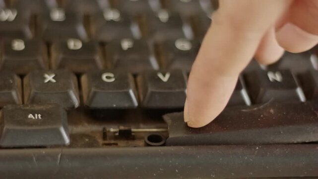 A person's finger repeatedly pressing a broken, snapped, and dusty computer keyboard spacebar button