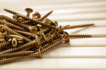 A pile of gold screws on a table made of wooden slats with warm lighting