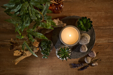 Fototapeta premium Candle on a stone surface surrounded by plants and decorative stones in a cozy indoor setting
