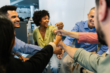 Group of smiling diverse professionals stacking fists in a circle, celebrating teamwork, collaboration and strong support. Teamwork and business concept