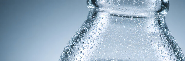 Close-up macro shot of condensation droplets on a clear, cold glass bottle conveying a refreshing and crisp feeling  