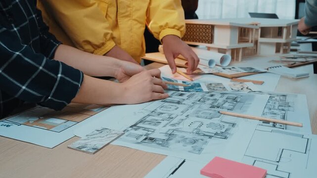 A group of architects collaborates in a bright office space, analyzing detailed blueprints and design plans on a table filled with tools and visual aids. SACTR