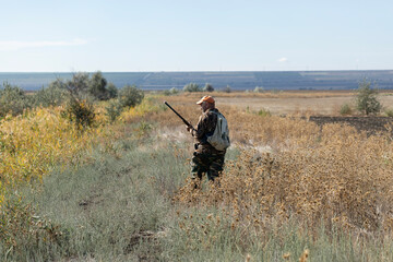 A hunter with a gun in camouflage clothing. A senior man with a gun, medium shot, searching for game.
