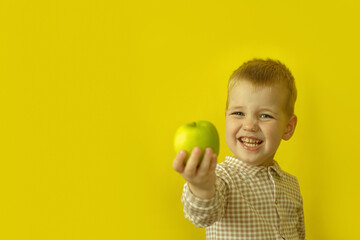 A happy boy with a green apple on a bright yellow background. The concept of healthy eating, childhood, joy and simple pleasures.