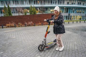 Parking electric scooter after daily commute in rainy city. Holding handlebars stops micromobility ride on wet pavement. Urban shared transport rental travel ends near sidewalk with drizzle today.