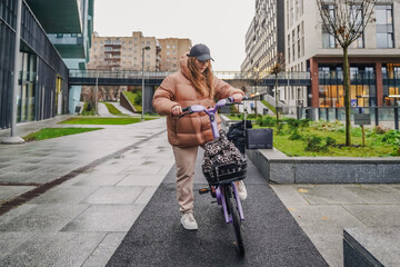 Parking rented electric bicycle after ride on wet pavement in rain. Inspecting basket, handlebars before next trip. Shared ebike rental supports commute, sustainable city transport, fitness travel.