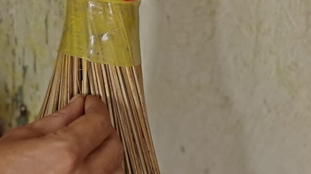 Hands inserting extra palm leaf ribs into a traditional broom to tighten and strengthen the bundle for cleaning