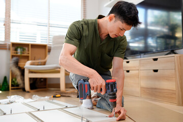 Man assembling purchased furniture in beautiful room with large window. Concept of DIY or furniture assembly services